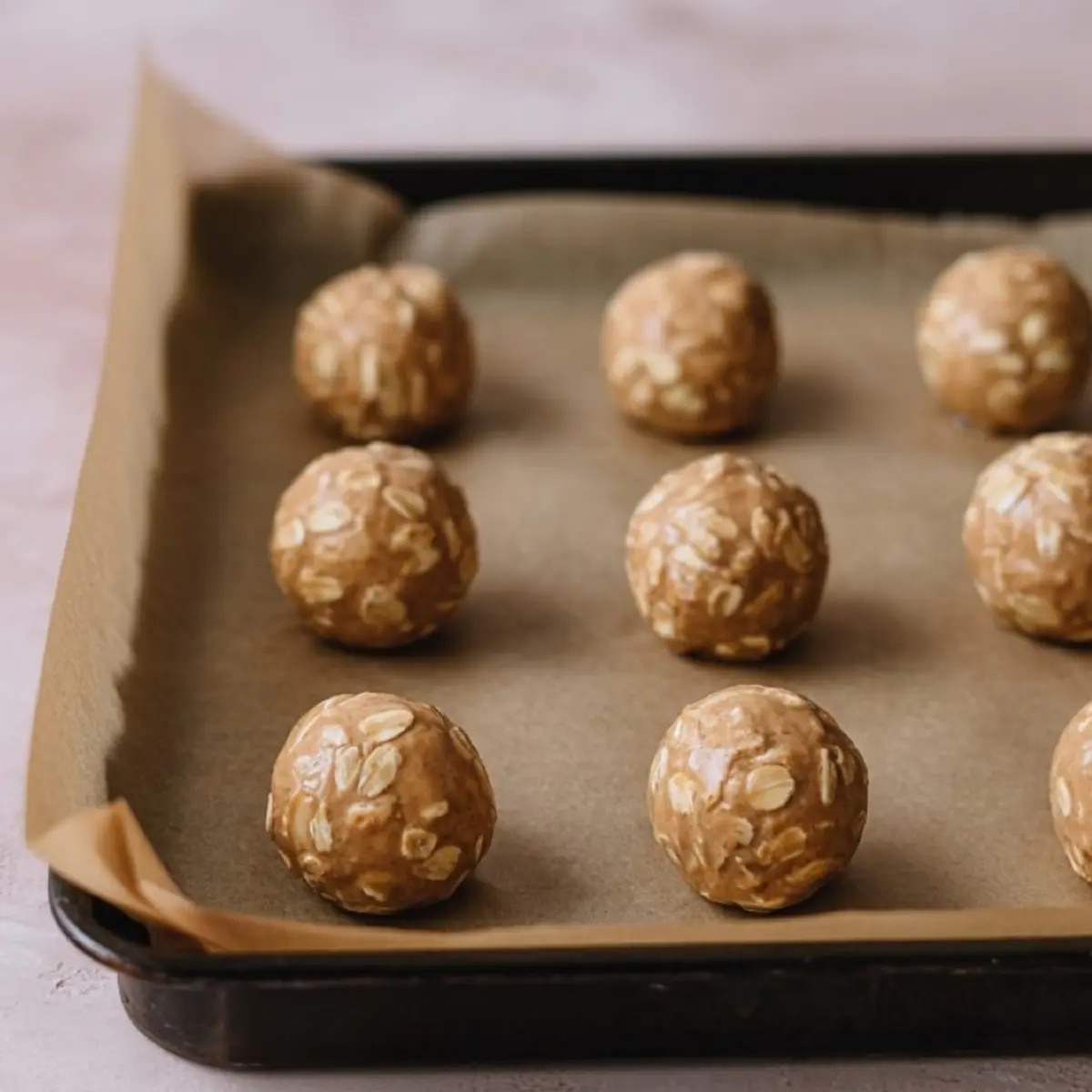 Rolled oat and peanut butter balls evenly spaced on a parchment-lined baking tray, ready for chilling or baking.