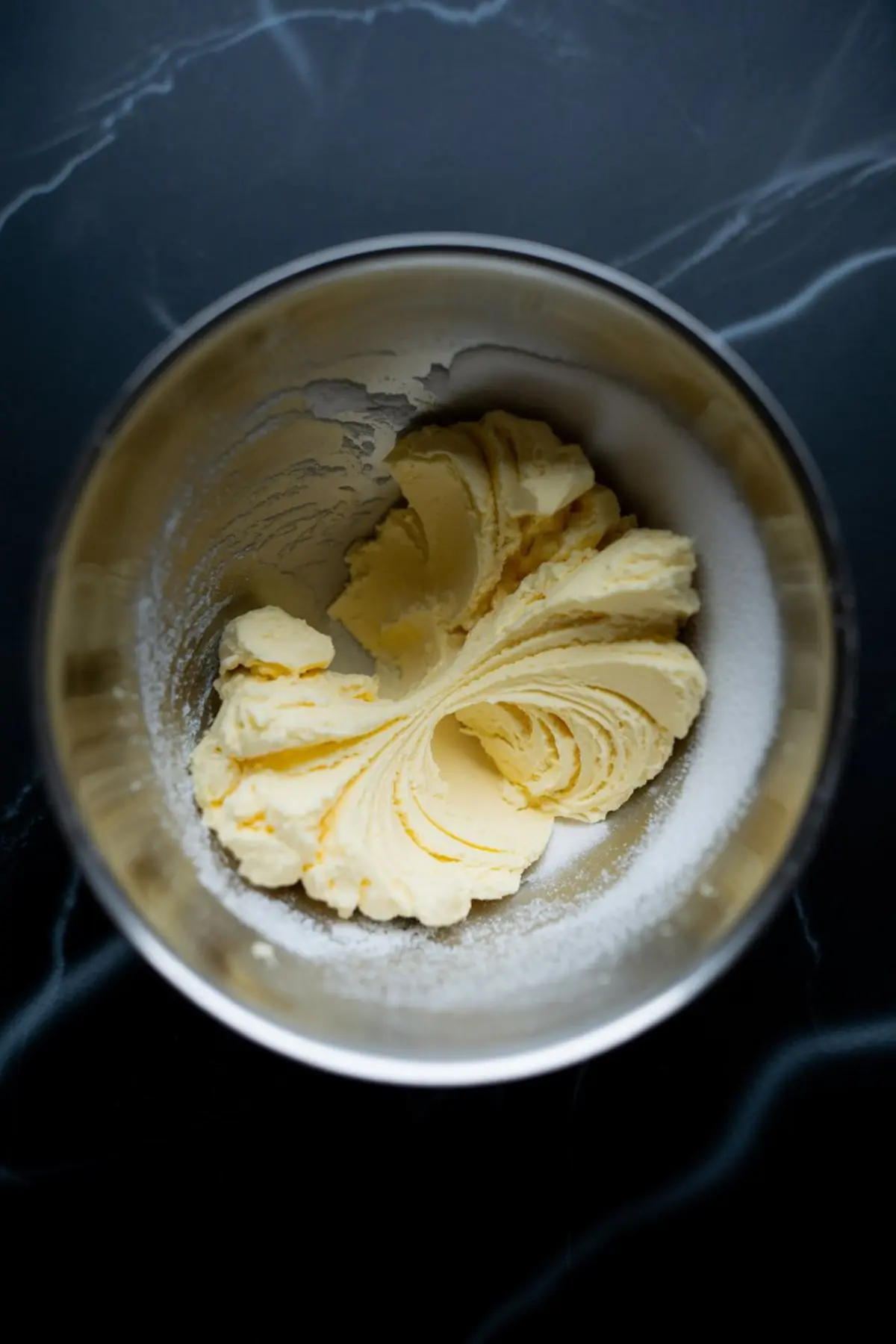 Softened butter and sugar creamed together in a stainless steel mixing bowl, forming smooth swirls ready for pistachio cupcake batter.