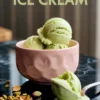Close-up of pistachio ice cream scoops in a pink ceramic bowl, with a scoop on a spoon and scattered crushed pistachios on the glossy black surface, captioned “Pistachio Ice Cream.”