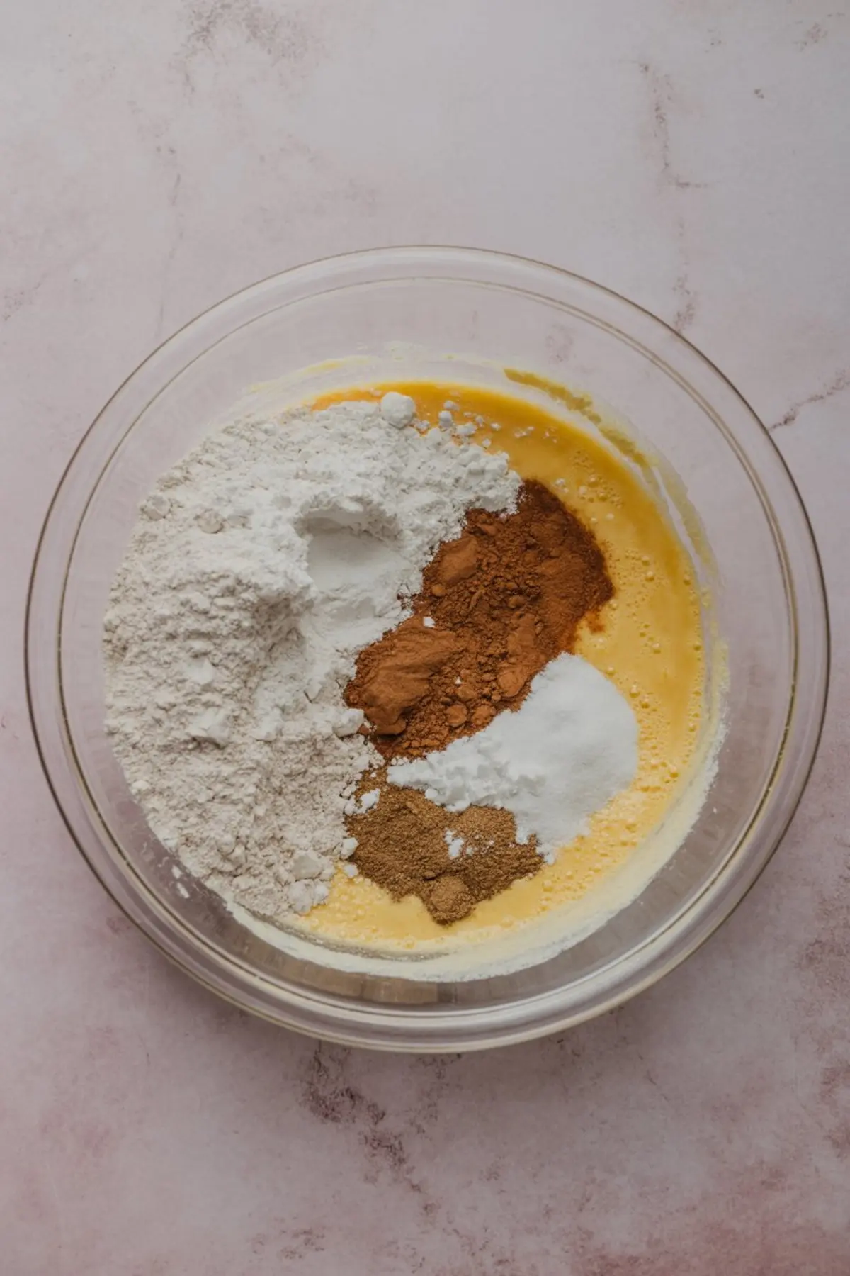 Glass mixing bowl containing flour, cinnamon, ginger, baking soda, and pumpkin puree, showing the dry and wet ingredients before mixing for pumpkin oatmeal cookies.