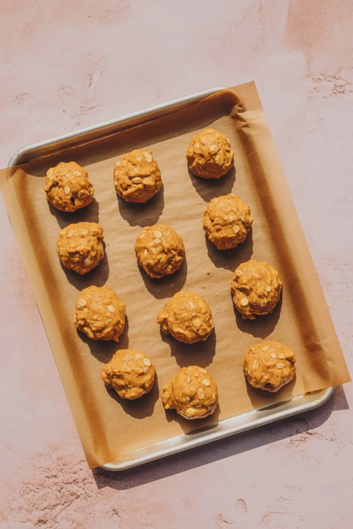 Baking sheet lined with parchment paper holding evenly spaced scoops of pumpkin oatmeal cookie dough ready for baking, captured under warm lighting.