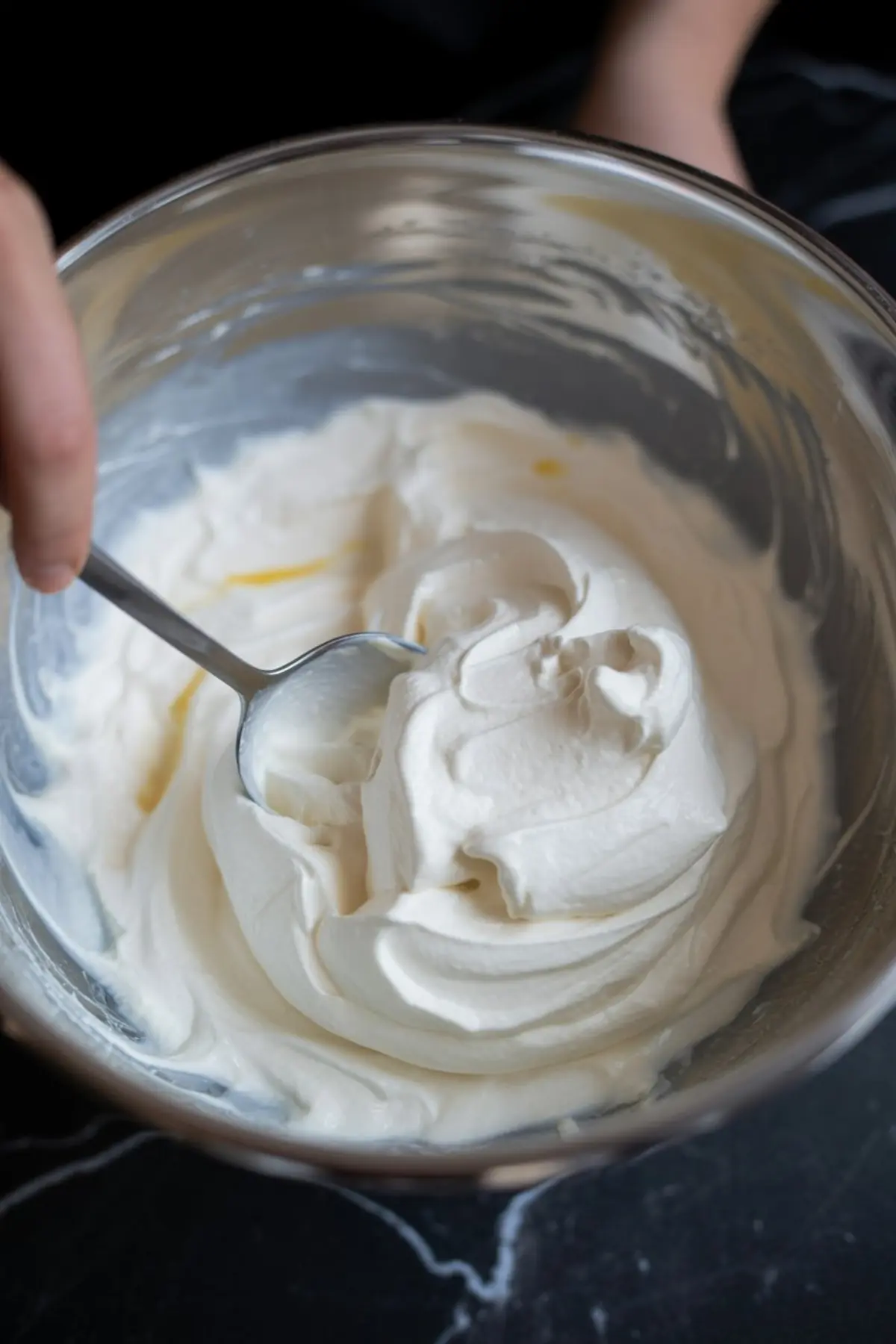 Bowl of freshly whipped cream being stirred with a spoon, creating a smooth and fluffy texture for dessert preparation.