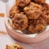 Stack of freshly fried apple fritters covered in cinnamon sugar, placed in a parchment-lined bowl with one fritter broken open to show the tender apple-filled interior.