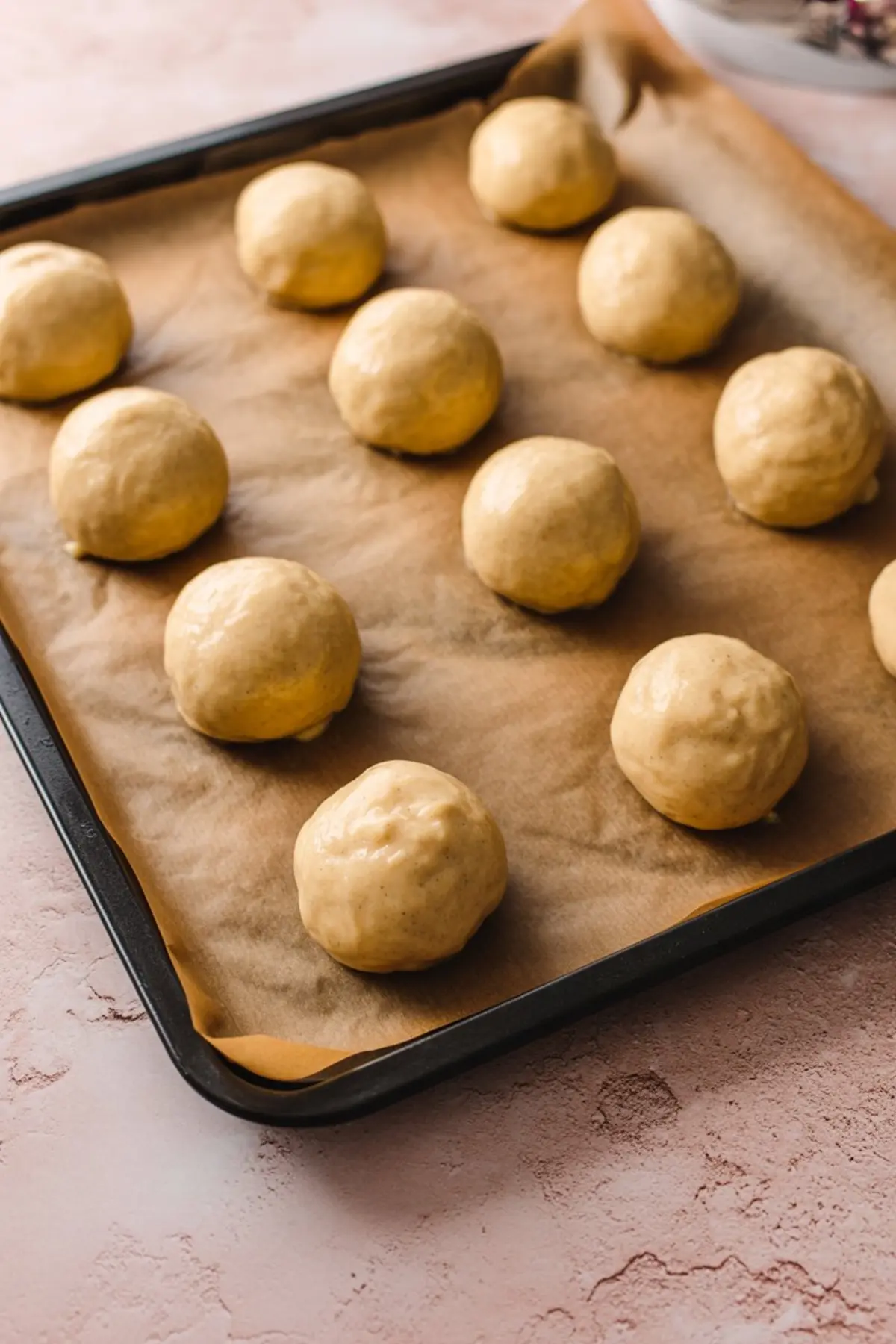 Tray of unbaked cookie dough balls on parchment paper, spaced evenly and ready to be baked into soft butterscotch cookies.
