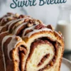 Front-facing slice of cinnamon swirl bread topped with vanilla glaze and pecans, placed on a white plate with milk in the background, highlighting the soft texture and caramelized cinnamon filling.