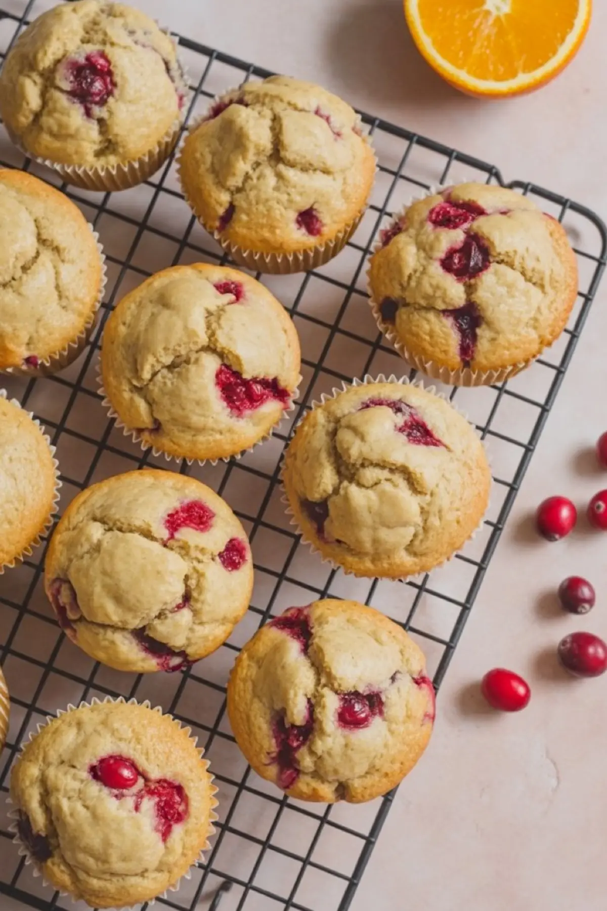 Freshly baked cranberry orange muffins cooling on a wire rack, with whole cranberries and half an orange nearby.