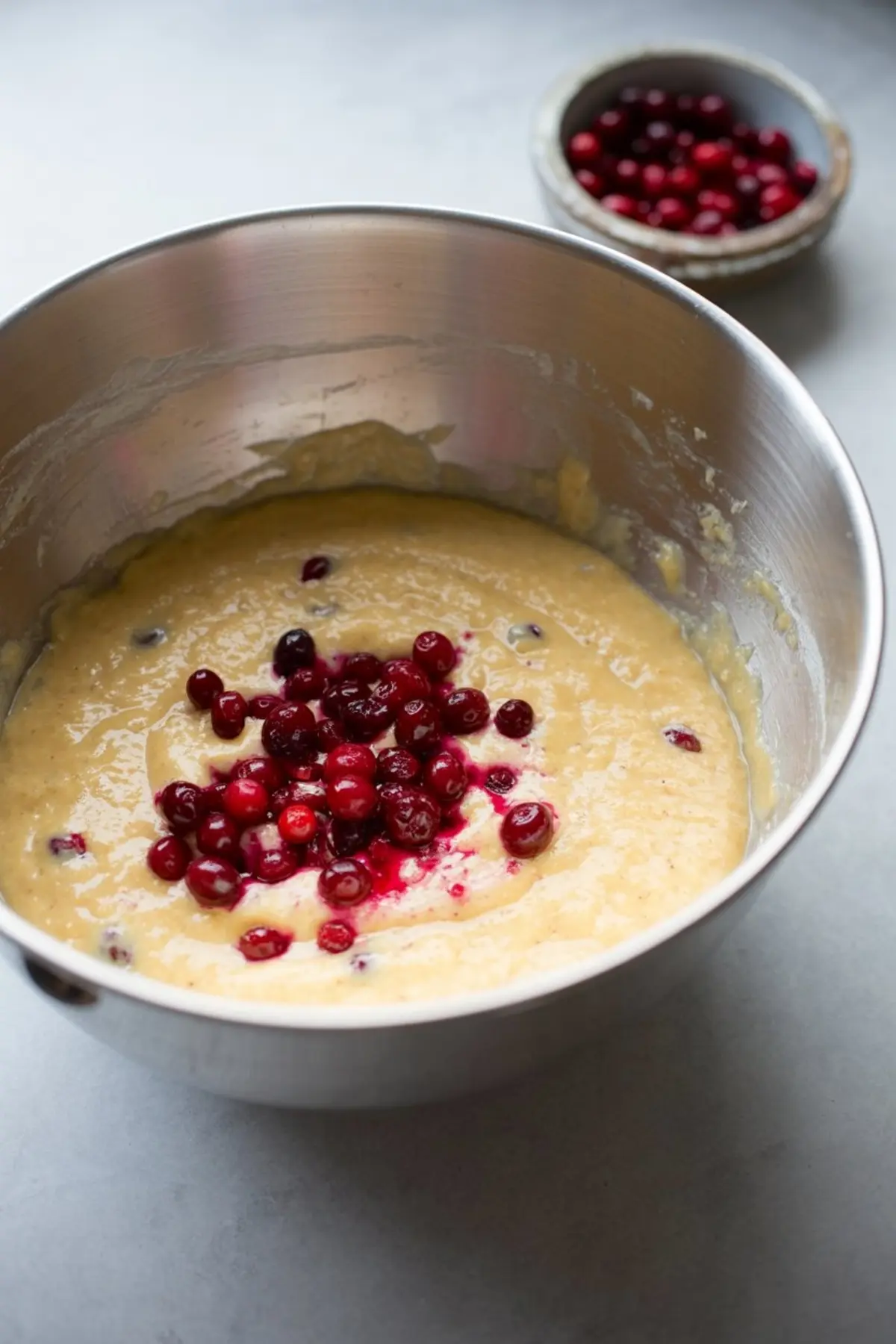 Batter in a stainless steel bowl with fresh cranberries folded in, ready to be mixed for cranberry orange muffins.