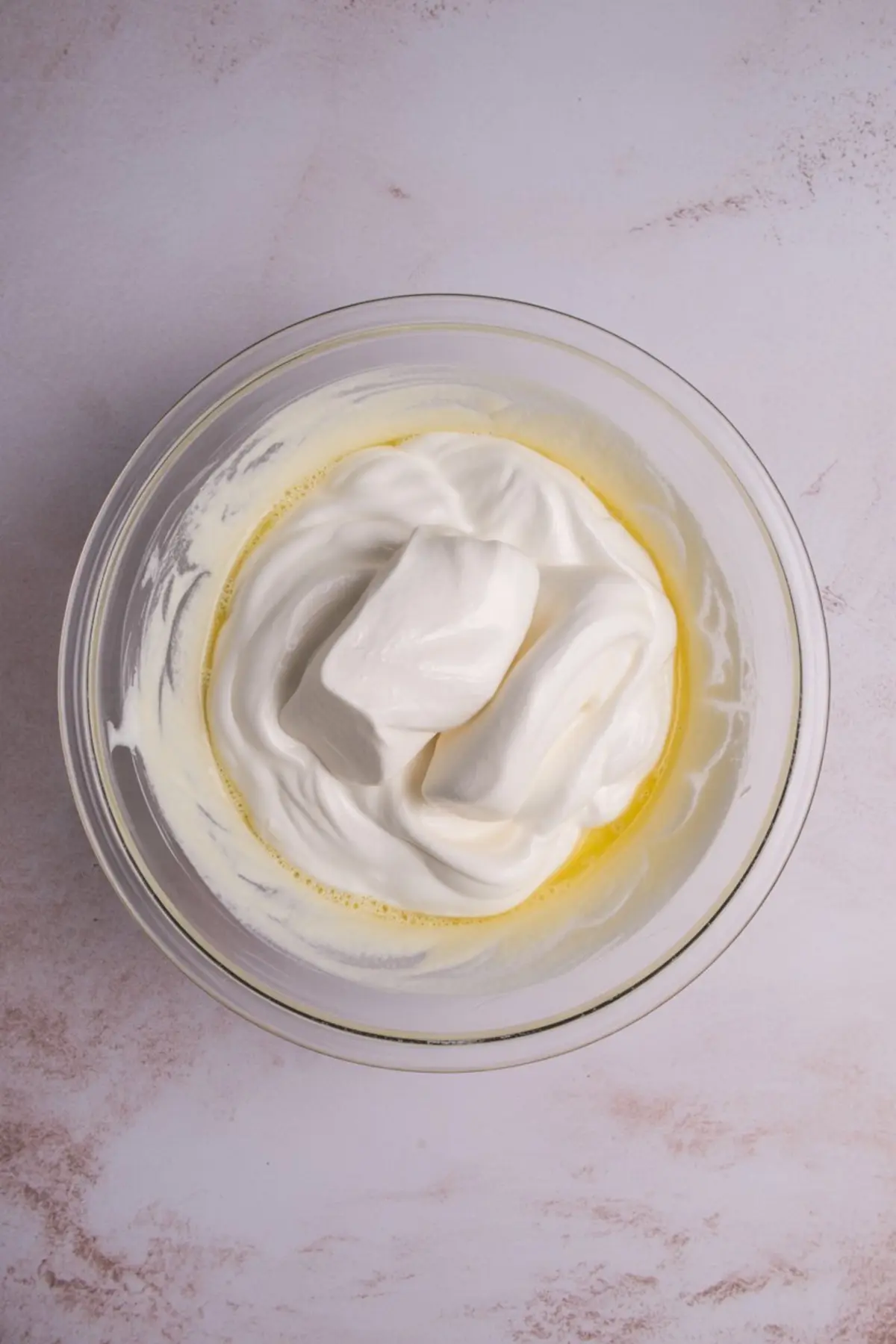 Glass mixing bowl filled with whipped topping and melted butter mixture on a light marble surface.