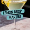 Lemon drop martini served in a sugar-rimmed martini glass, garnished with a lemon twist and placed on a pink marble surface, with bold black and blue label text reading “LEMON DROP MARTINI.”