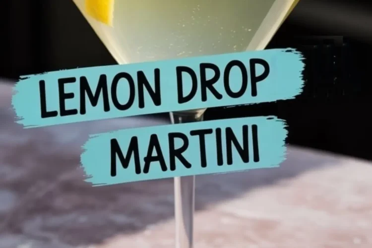 Lemon drop martini served in a sugar-rimmed martini glass, garnished with a lemon twist and placed on a pink marble surface, with bold black and blue label text reading “LEMON DROP MARTINI.”