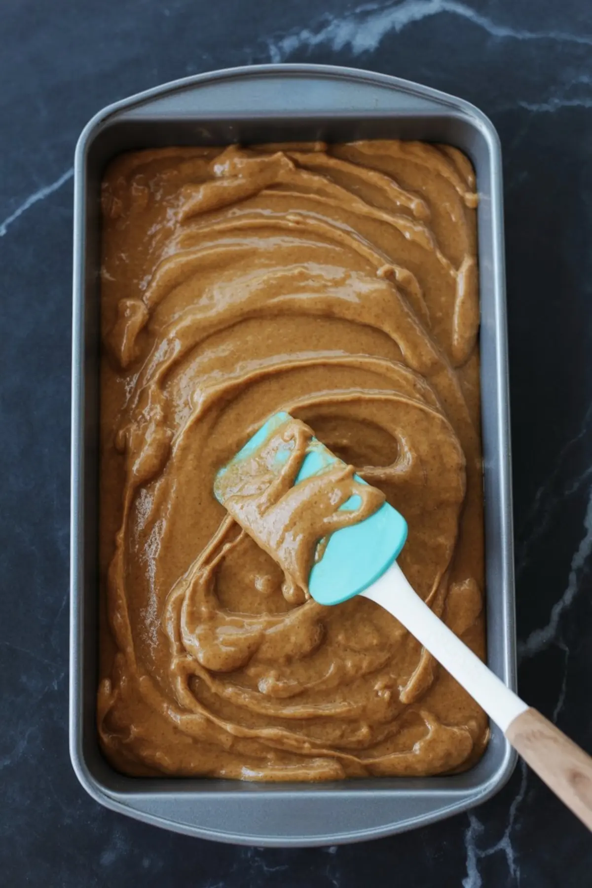 Pumpkin batter being spread evenly in a loaf pan with a silicone spatula.