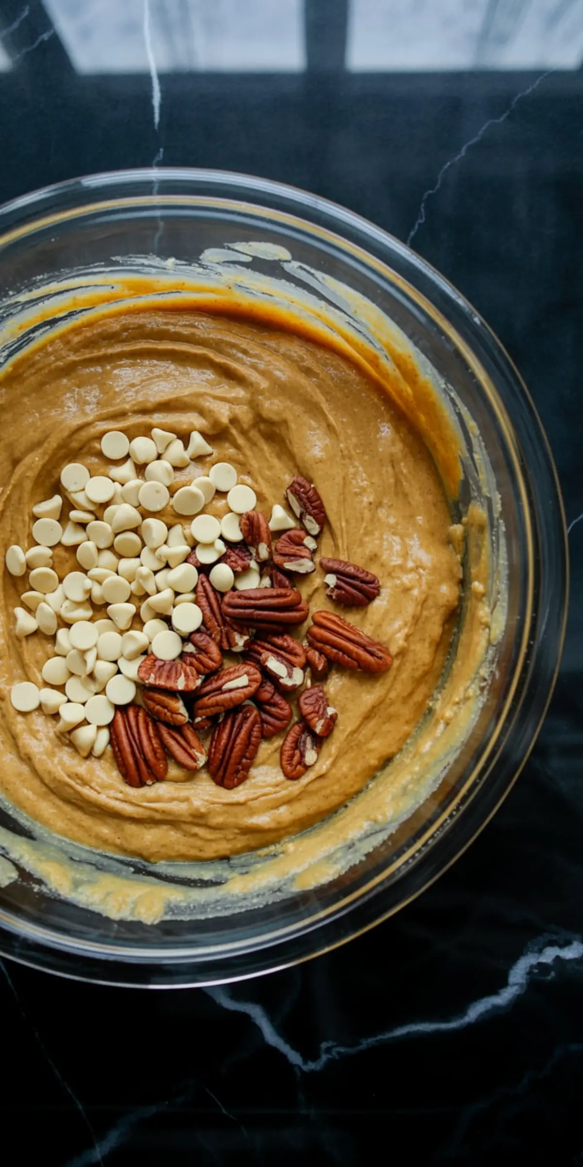 Bowl of spiced pumpkin cookie dough topped with white chocolate chips and raw pecan halves before final mixing.