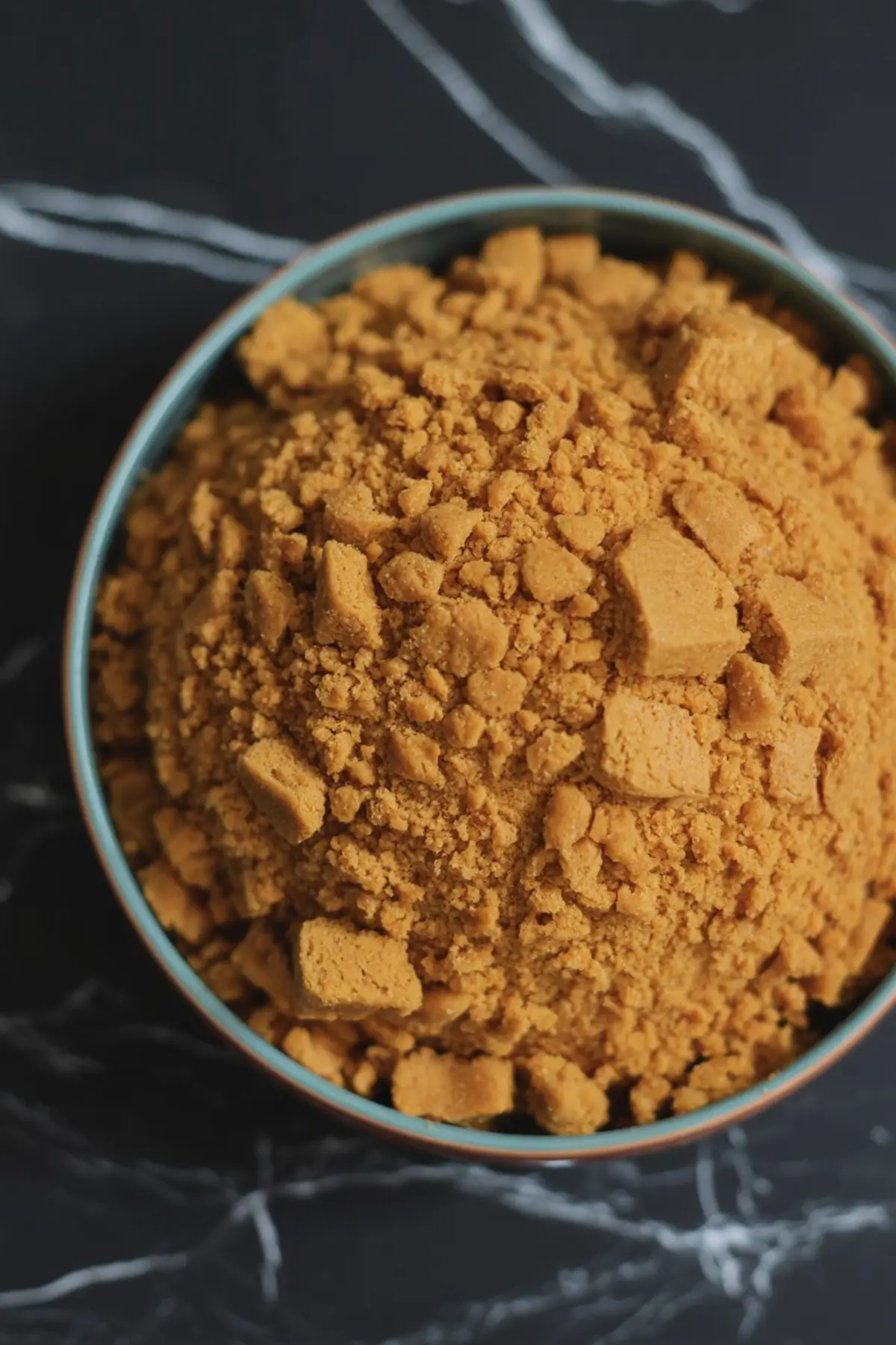 Crushed gingersnap cookie crumbs in a blue-rimmed bowl, showcasing coarse and fine textures, perfect for fall dessert bases or no-bake crusts.