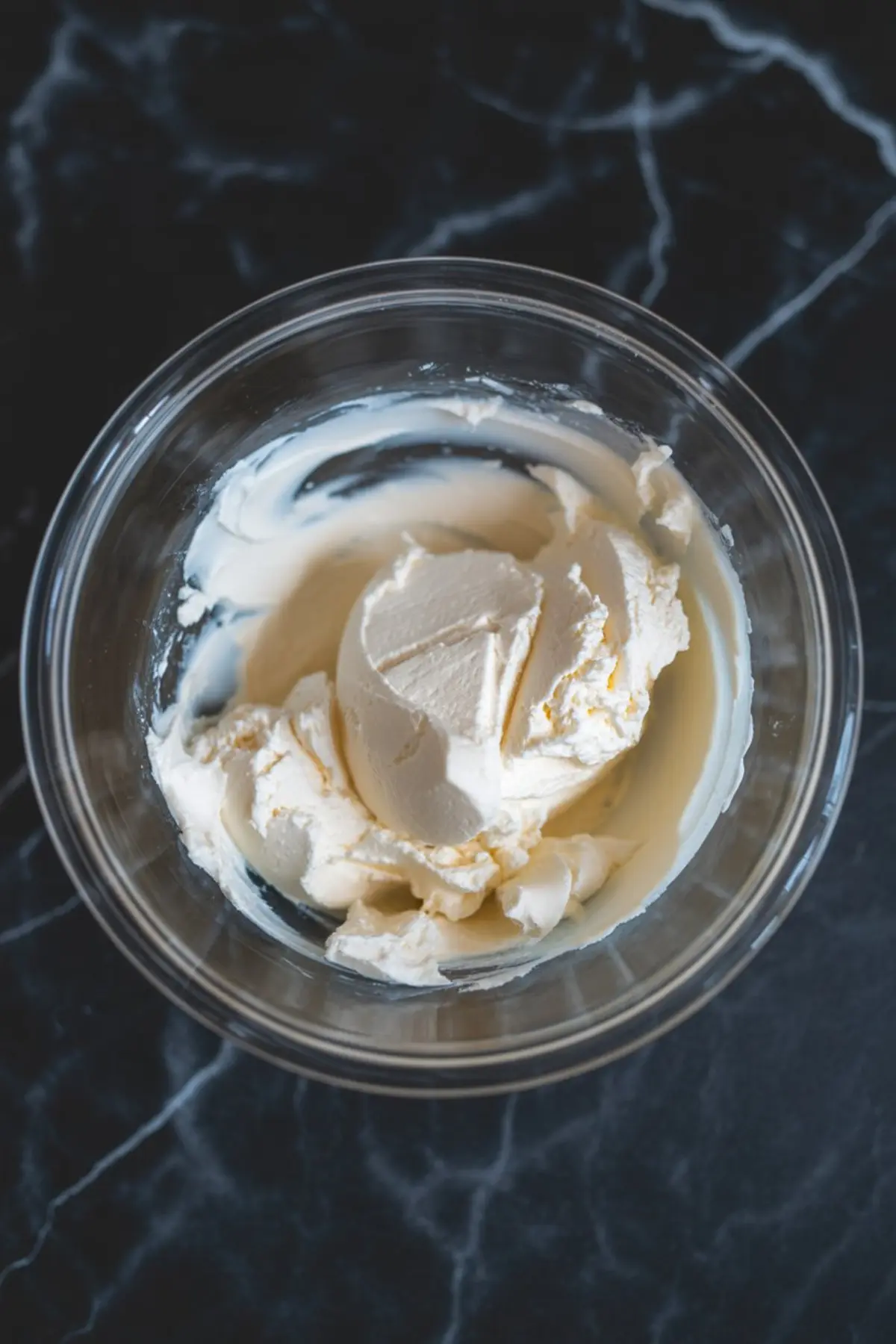 Overhead view of cream cheese in a mixing bowl, softened and slightly whipped, prepared for blending. This step emphasizes the creamy base used in making pumpkin cream cheese spread.
