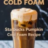 A tall glass of iced pumpkin cold foam coffee with creamy foam spilling over the rim, labeled as “Starbucks Pumpkin Cold Foam Recipe” in bold font over a black marble backdrop.