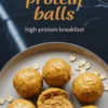 Plate of glossy pumpkin protein balls with one sliced open to reveal a moist, dense texture, surrounded by scattered oats on a black marble background, with text overlay promoting high protein breakfast.