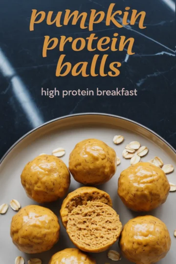 Plate of glossy pumpkin protein balls with one sliced open to reveal a moist, dense texture, surrounded by scattered oats on a black marble background, with text overlay promoting high protein breakfast.
