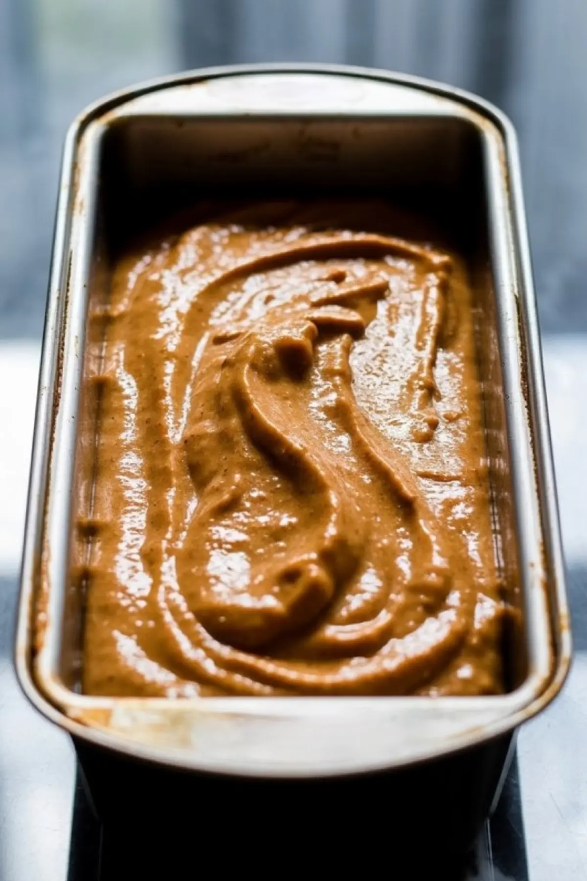 Unbaked vegan pumpkin bread batter spread evenly in a loaf pan, showing its rich golden-brown color and thick consistency before going into the oven.
