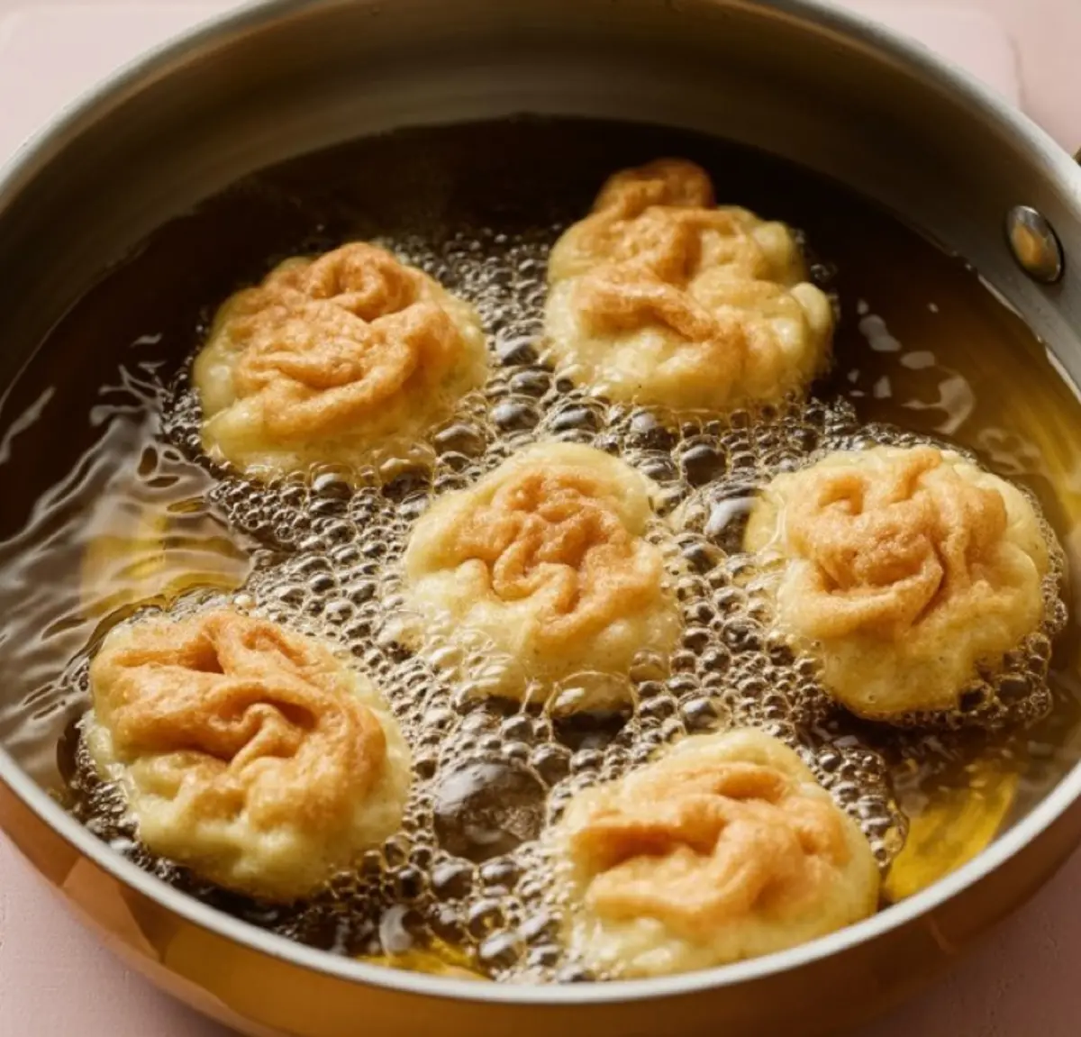 Apple fritters frying in bubbling oil inside a skillet, showcasing the golden crust forming during the cooking process.
