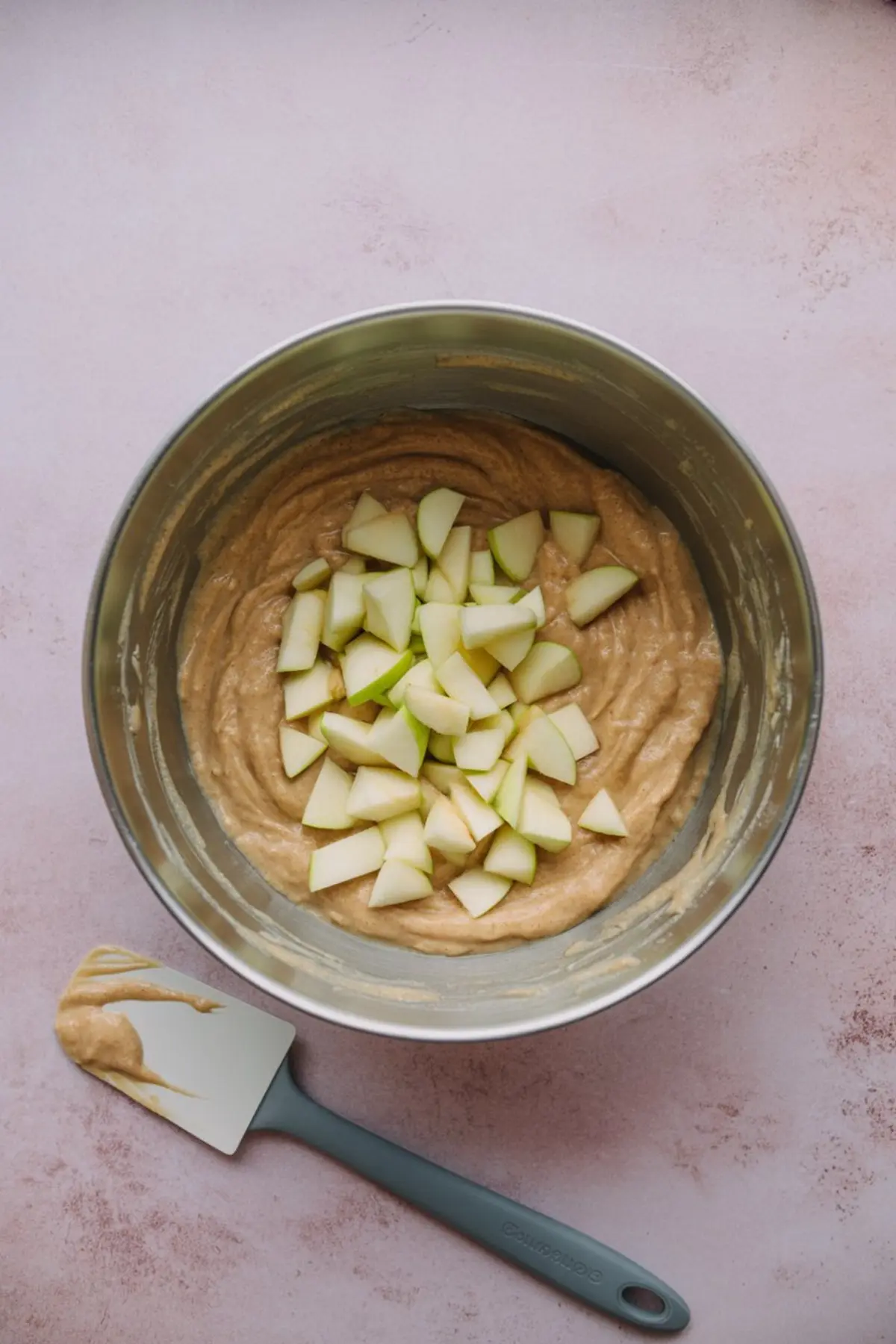 Chopped green apples added to a thick cinnamon-spiced batter inside a large mixing bowl, prepared for making homemade apple fritters.
