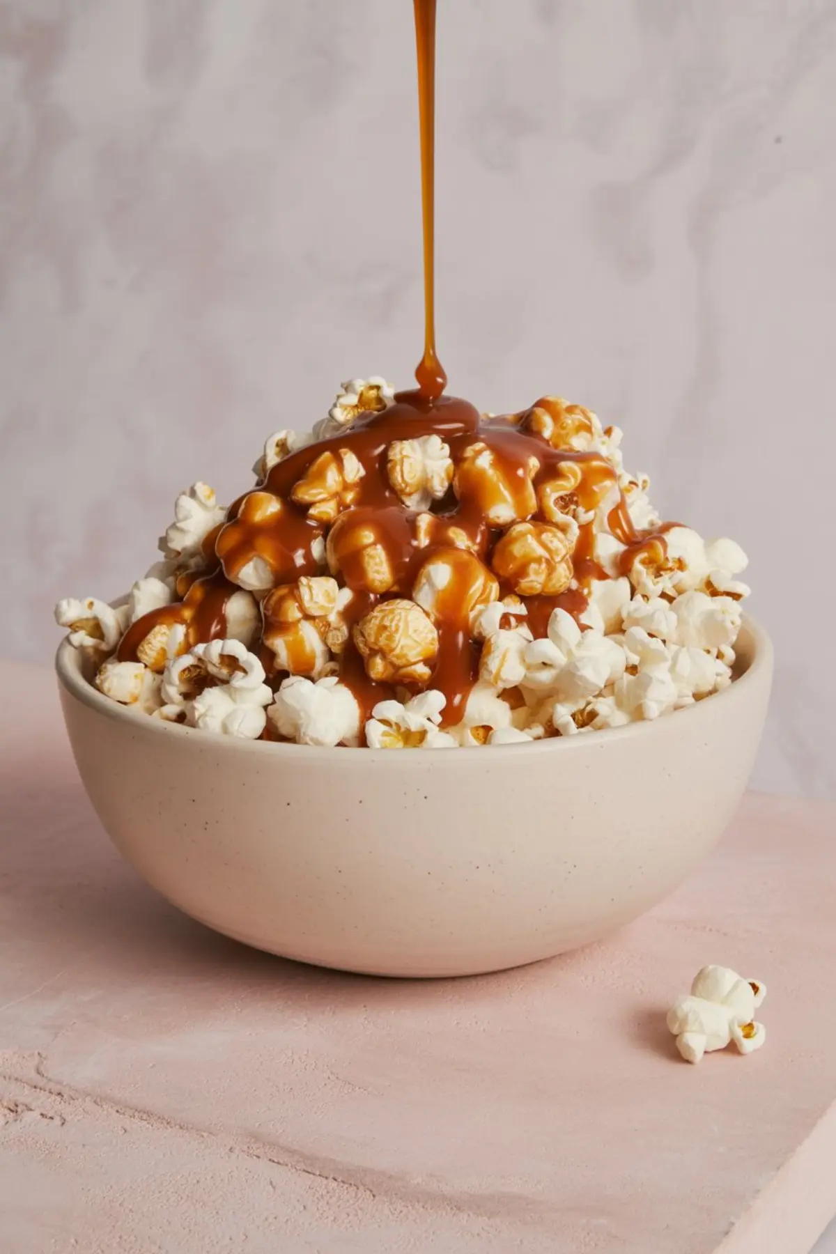Caramel sauce being drizzled over a bowl of freshly popped popcorn, creating a gooey and sweet coating on the kernels for a rich caramel popcorn treat.
