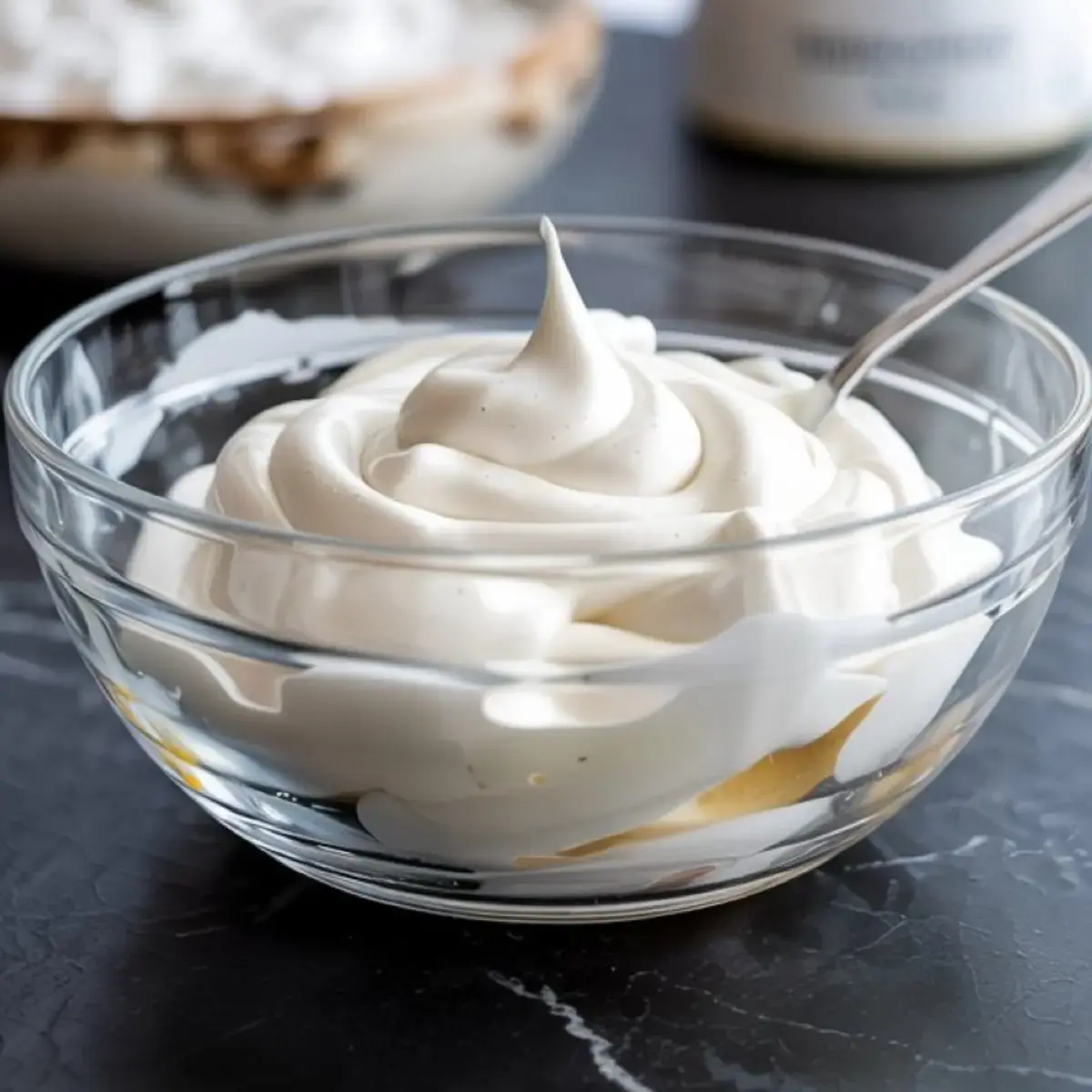 Fluffy white royal icing swirled in a glass bowl with a spoon, prepared for decorating gingerbread cookies and holiday desserts.
