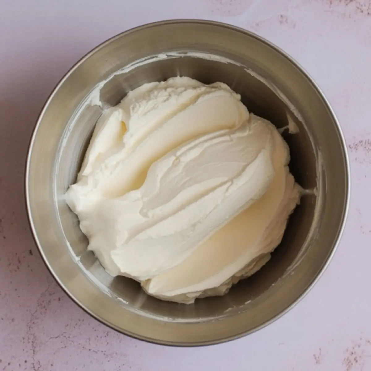 Stainless steel bowl filled with freshly whipped cream cheese frosting, featuring a soft, spreadable texture and smooth consistency, ideal for icing cakes or cupcakes.