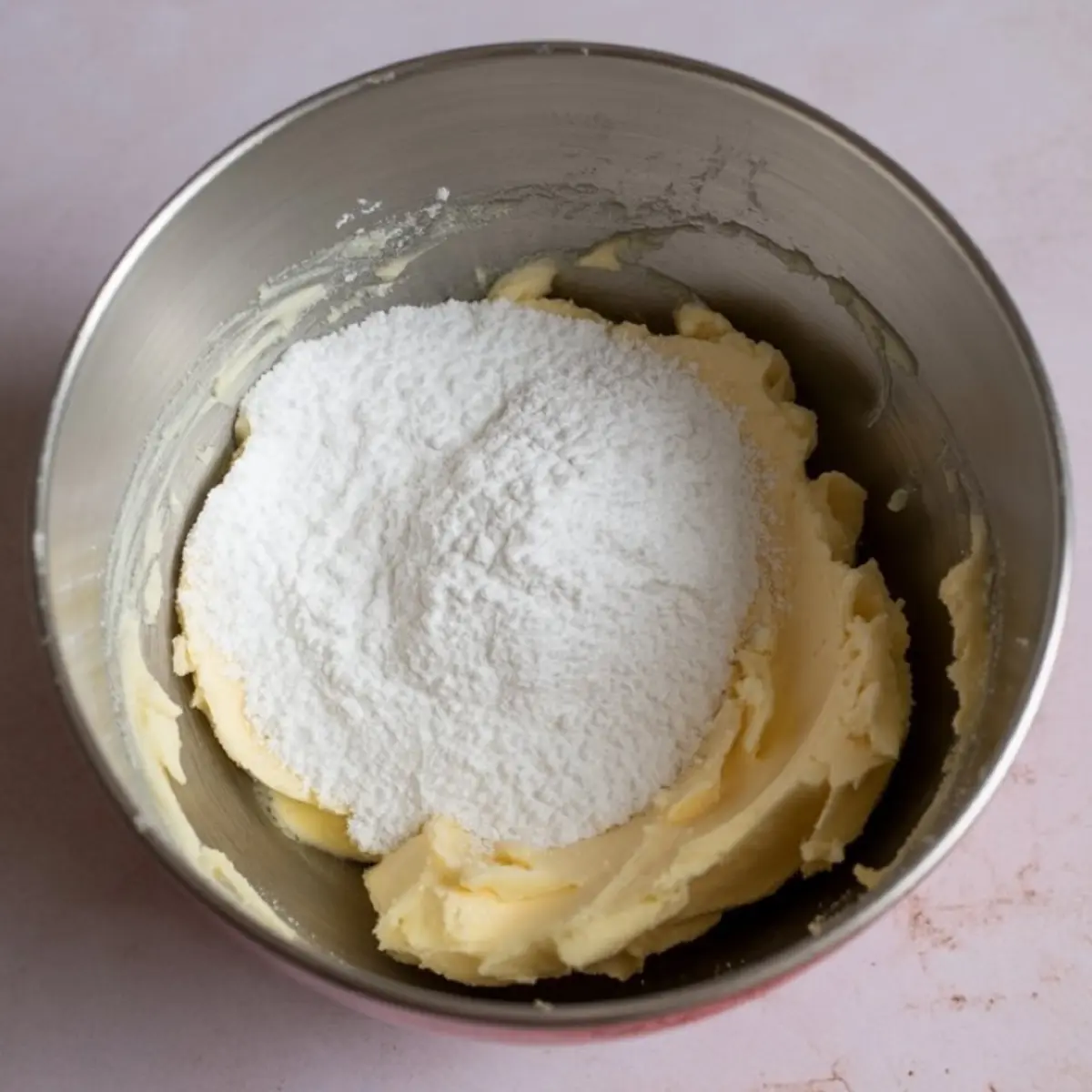 Unmixed ingredients in a metal bowl showing butter and powdered sugar before blending, part of a cream cheese frosting recipe ideal for beginners.