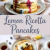 Fluffy lemon ricotta pancakes stacked with layers of cream and blueberry sauce, topped with lemon zest, whipped topping, and maple syrup, surrounded by blueberries, lemon slices, and pastel-toned tableware on a marble background.