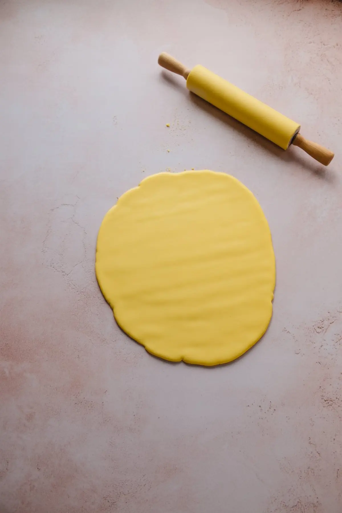 Yellow fondant rolled out flat with a matching yellow rolling pin on a lightly floured pink surface, ready for cutting decorative accents.
