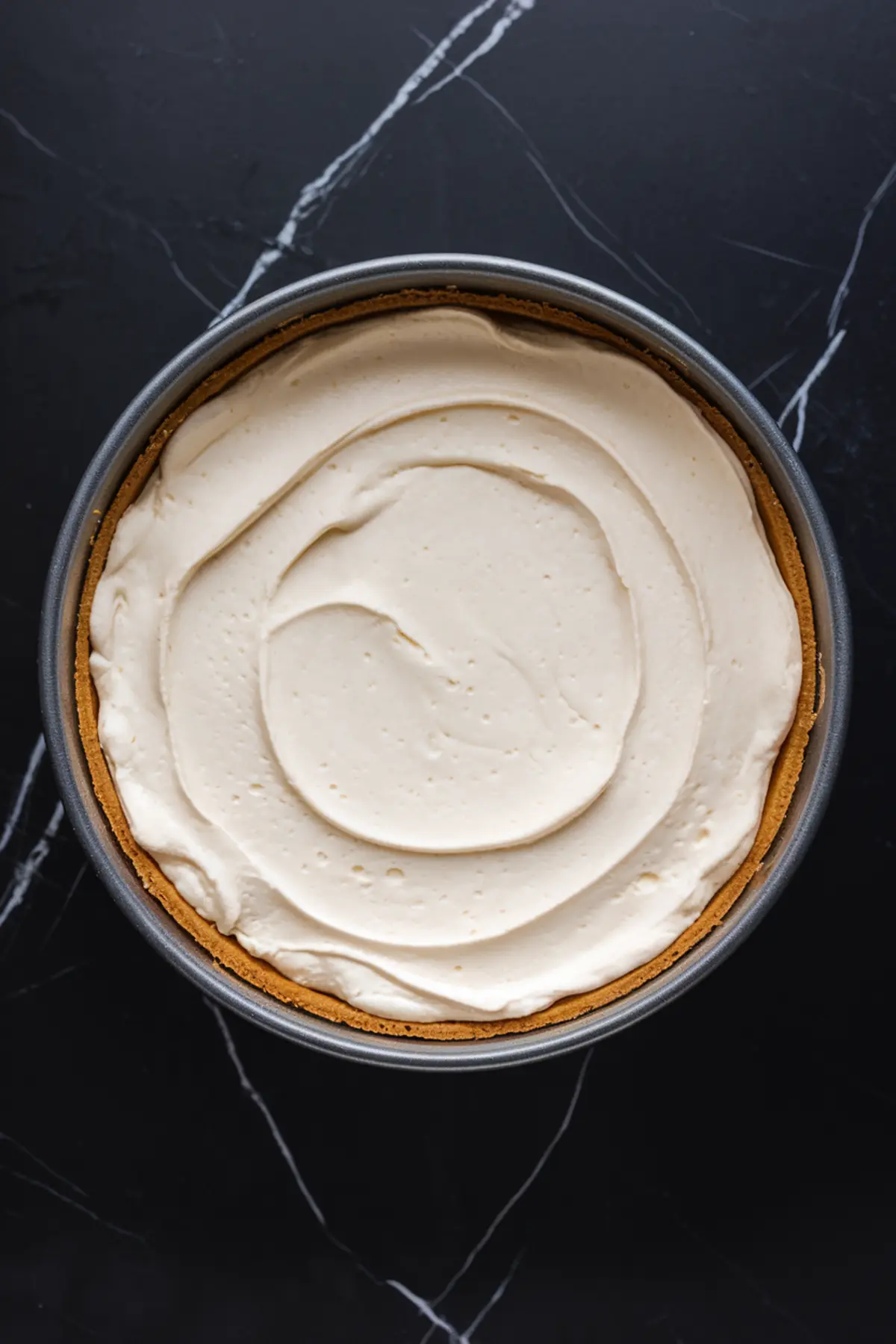 Unbaked cheesecake in a springform pan with a graham cracker crust and a thick, swirled cream cheese filling, ready for blueberry topping or lemon blueberry cheesecake variations.
