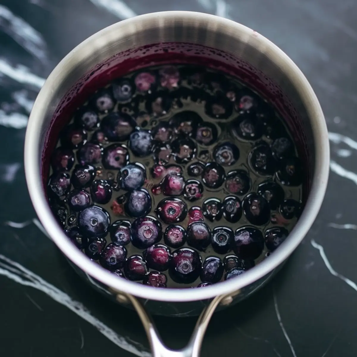 Fresh blueberries simmering in a saucepan to create a glossy homemade blueberry sauce, perfect for blueberry desserts and cheesecake with blueberry topping.
