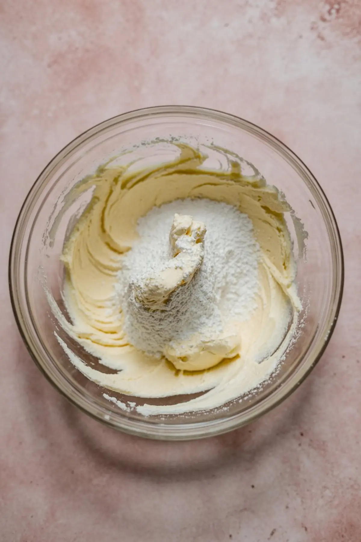 Butter mixture whipped light in a glass bowl, snowy mound of powdered sugar piled on top before blending.