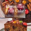 Classic holiday fruit cake decorated with vibrant red and green glacé cherries, golden jellies, and pecans, sliced to display a moist, fruit-packed crumb.