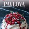 Decorated Christmas pavlova topped with sugared cranberries, blueberries, raspberries, and fresh rosemary sprigs, with red berry sauce dripping over a crisp white meringue base on a dark background.