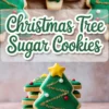 Decorated Christmas tree sugar cookies stacked on a white plate with green royal icing, gold glittery garland, red and white candy ornaments, and a yellow star topper, with overlay text reading “Christmas Tree Sugar Cookies.”