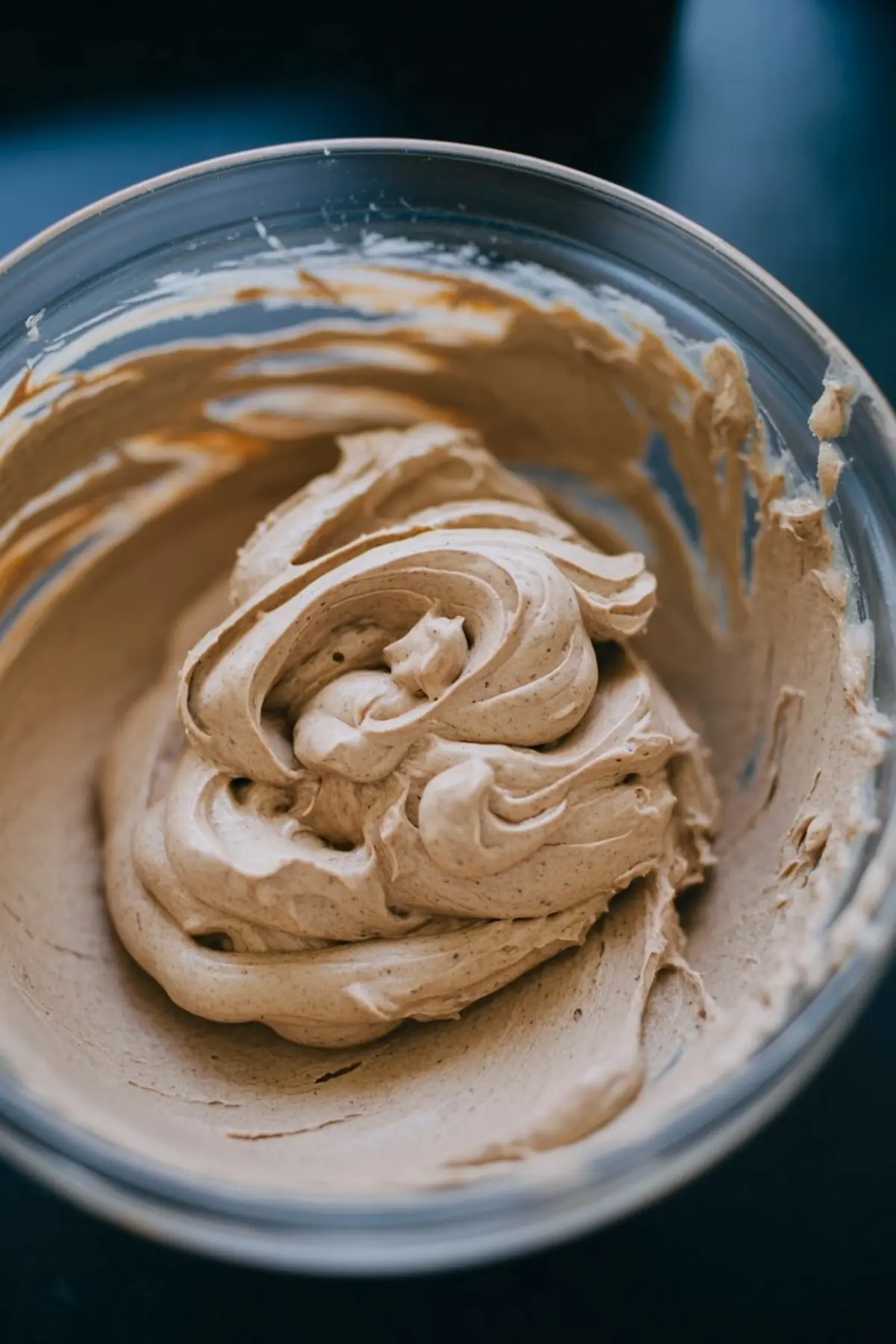 Thick cookie dough frosting swirled in a glass mixing bowl, showcasing its rich and creamy texture with visible flecks of brown sugar and vanilla.