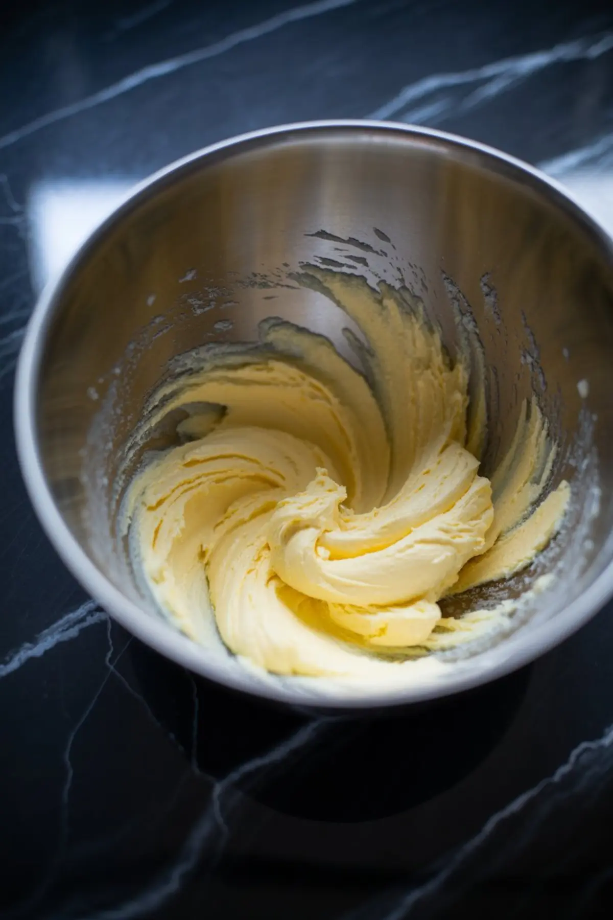 A bowl of creamed butter whipped to a light and fluffy consistency, ready for the next stage of frosting preparation.
