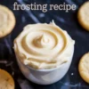 A swirl of vanilla frosting piped into a white bowl, surrounded by plain sugar cookies on a black marble surface. Overlay text reads “cookie frosting recipe.”