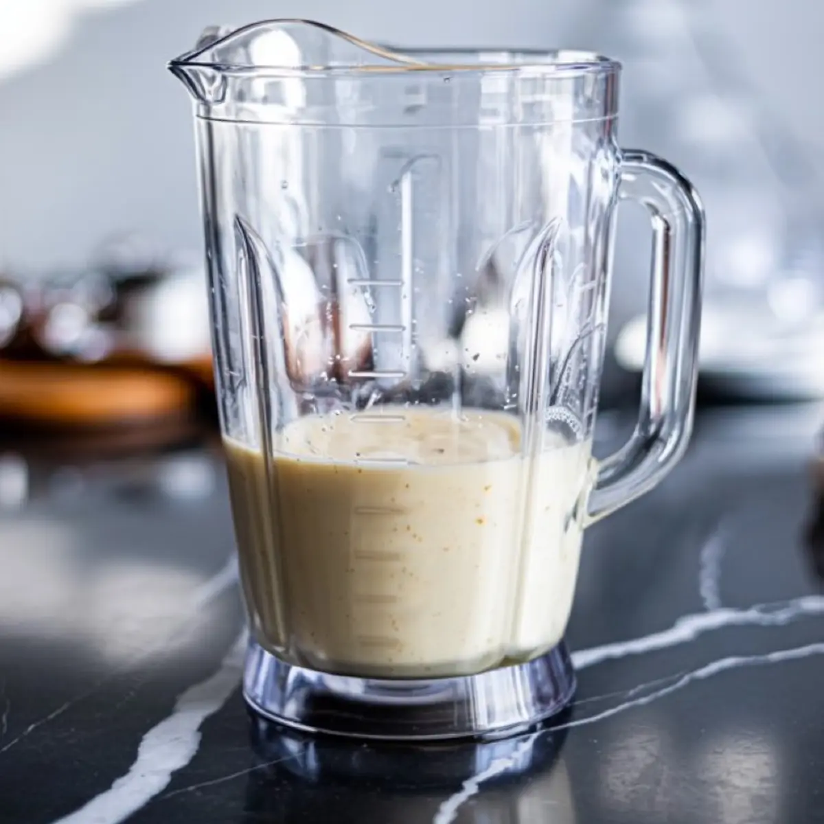 Blender jar filled with creamy pancake batter sitting on a black marble counter, ready for pouring into a hot pan.
