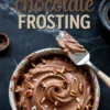 Swirled bowl of German chocolate frosting garnished with chopped pecans and coconut flakes, with a metal spatula resting on top, and stylized “German Chocolate Frosting” text on dark background.