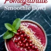 Top-down view of a vibrant pomegranate smoothie bowl with shredded coconut, pomegranate arils, and toasted coconut flakes, garnished with mint and framed by a holiday-themed text overlay on a marble surface.