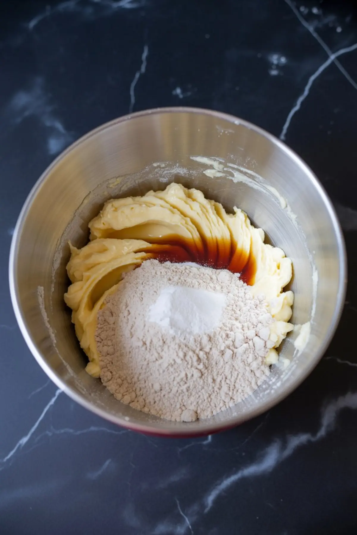 A mixing bowl filled with cookie dough ingredients, including creamed butter, vanilla extract, flour, and baking powder, ready to be combined for maple brown sugar thumbprint cookies.

