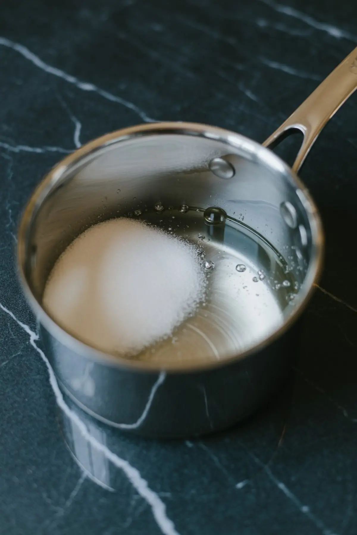 Granulated sugar combined with liquid ingredients in a stainless steel saucepan, ready to be heated into sugar syrup for marshmallow frosting.
