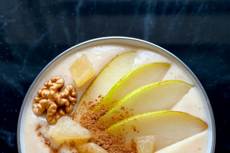 Overhead shot of a pear ginger smoothie bowl garnished with sliced pear, cinnamon, pineapple chunks, and whole walnuts on a black marbled background, with a title text overlay.
