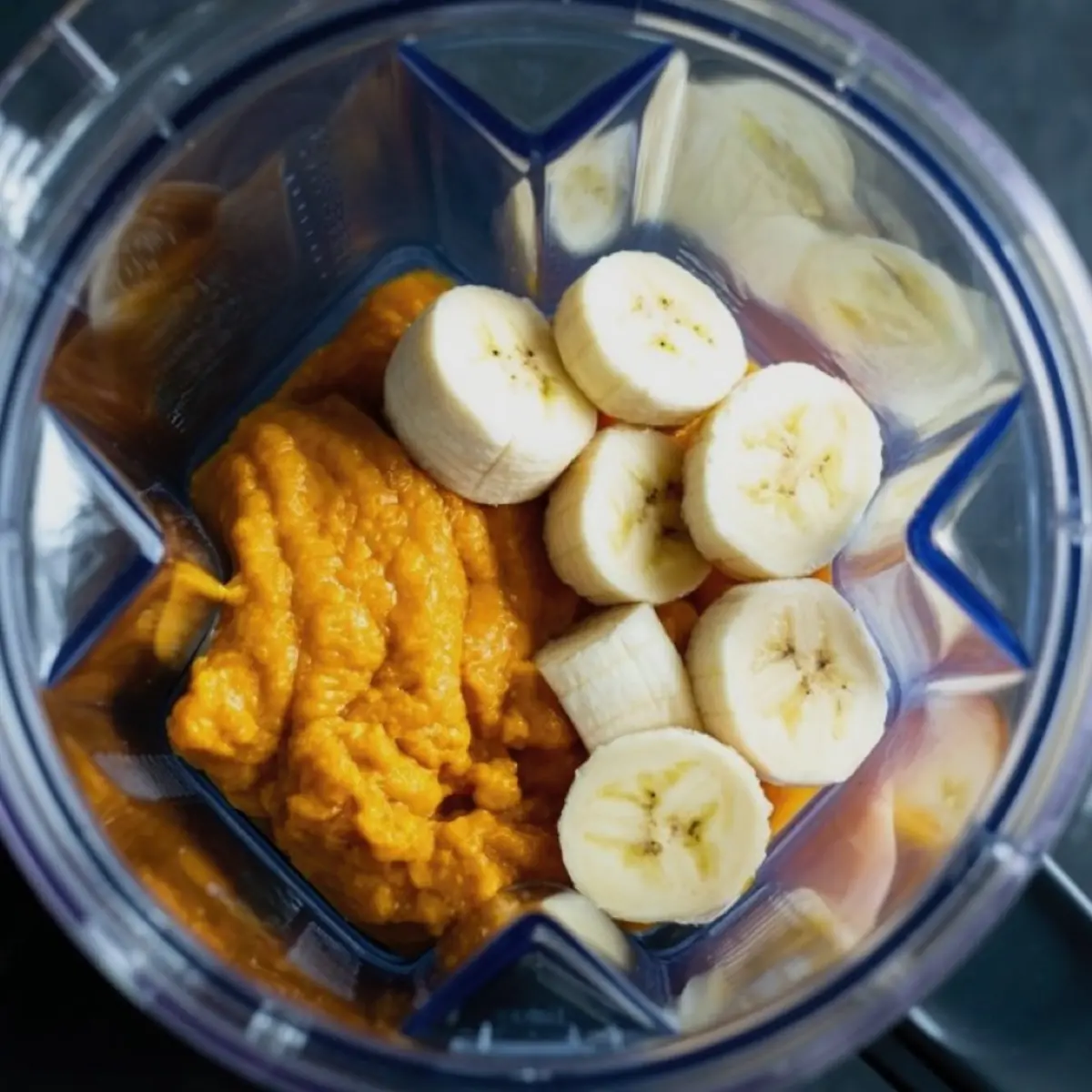 Close-up of a blender filled with sliced bananas and pumpkin puree, prepared for blending into a smoothie base.
