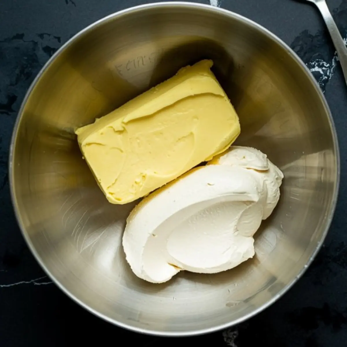Block of vegan butter and scoop of plant-based cream cheese in a stainless steel mixing bowl, prepared for dairy-free frosting.