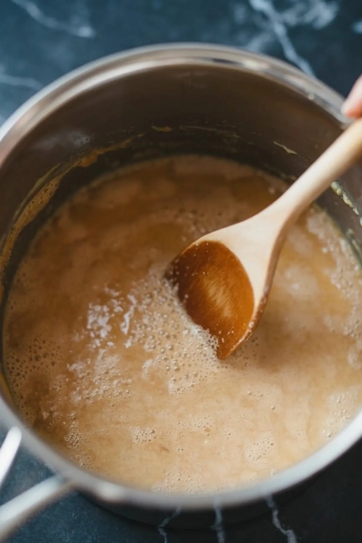 Brown mixture bubbling in a saucepan with a wooden spoon stirring it, showing the cooking process of the custard base for the chocolate pots.