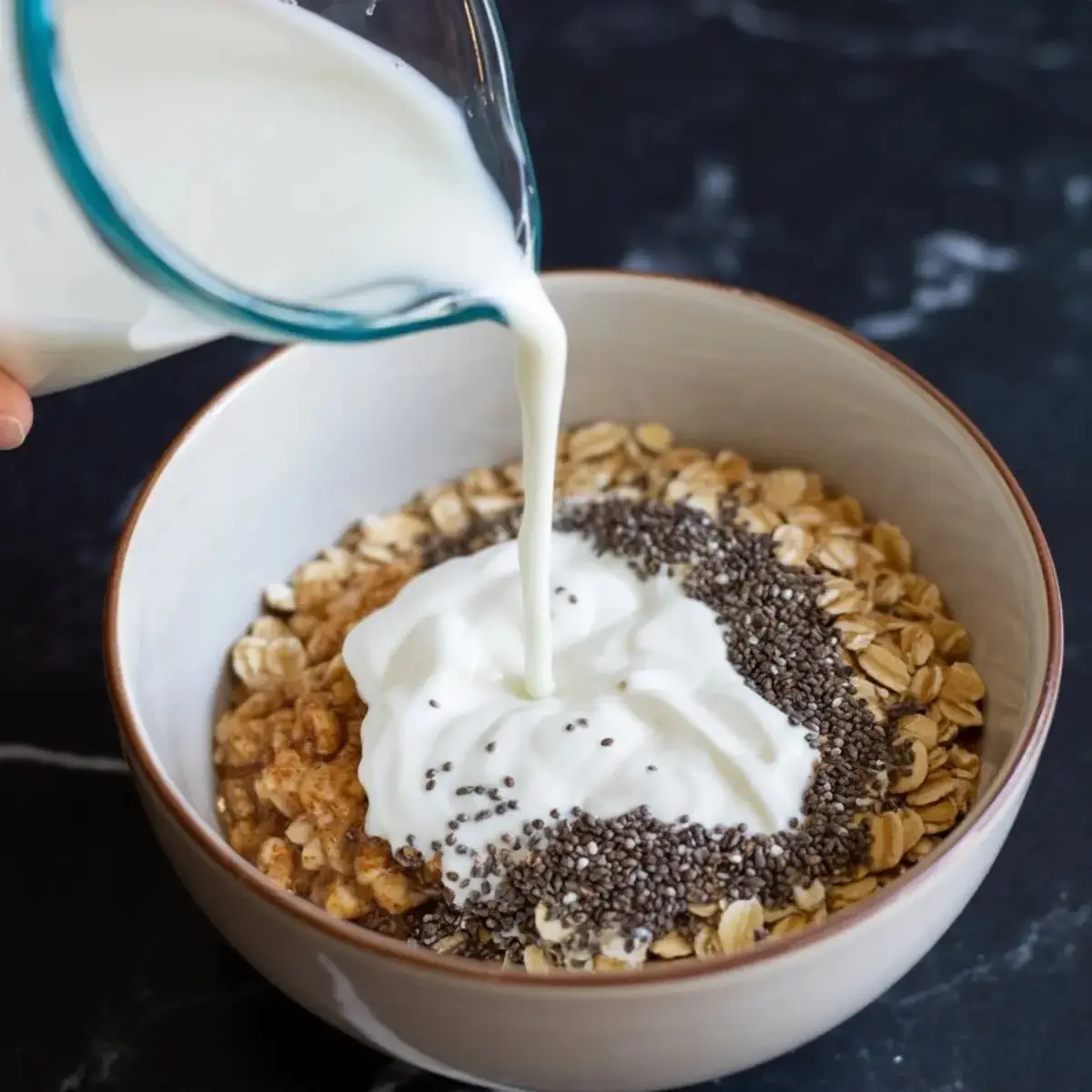 Milk being poured into a bowl filled with rolled oats, plain yogurt, chia seeds, and cinnamon, creating a wholesome base for overnight oats.