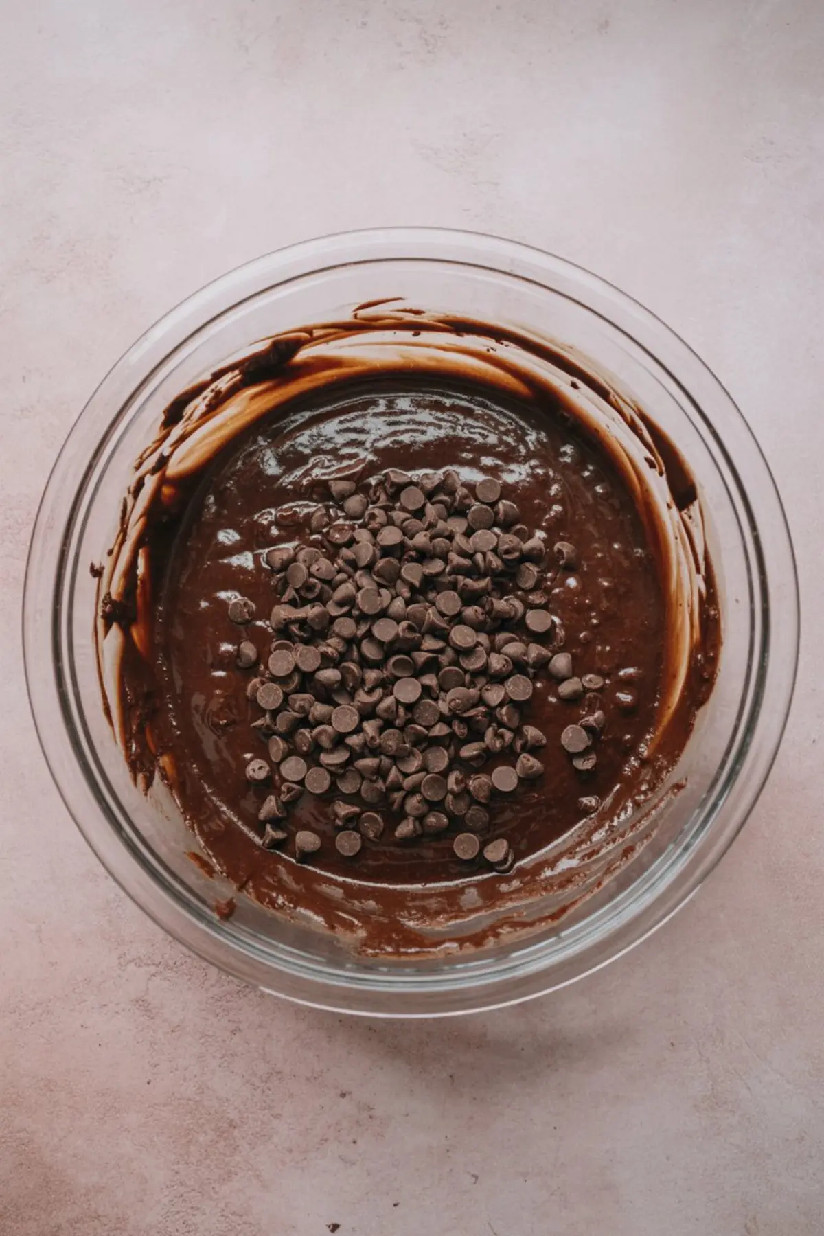 Thick brownie batter in a mixing bowl with chocolate chips added on top, ready to be folded in for a rich and gooey texture.